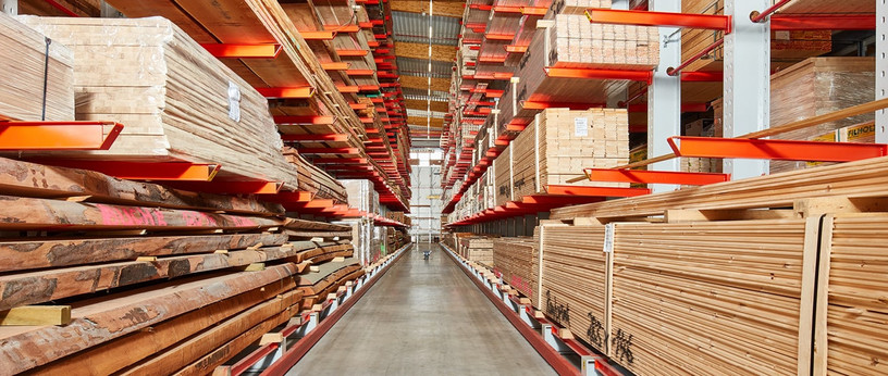 Großes Holzlager mit gestapeltem Schnittholz, Kanthölzern und Brettern in hohen Regalen mit roten Trägern.