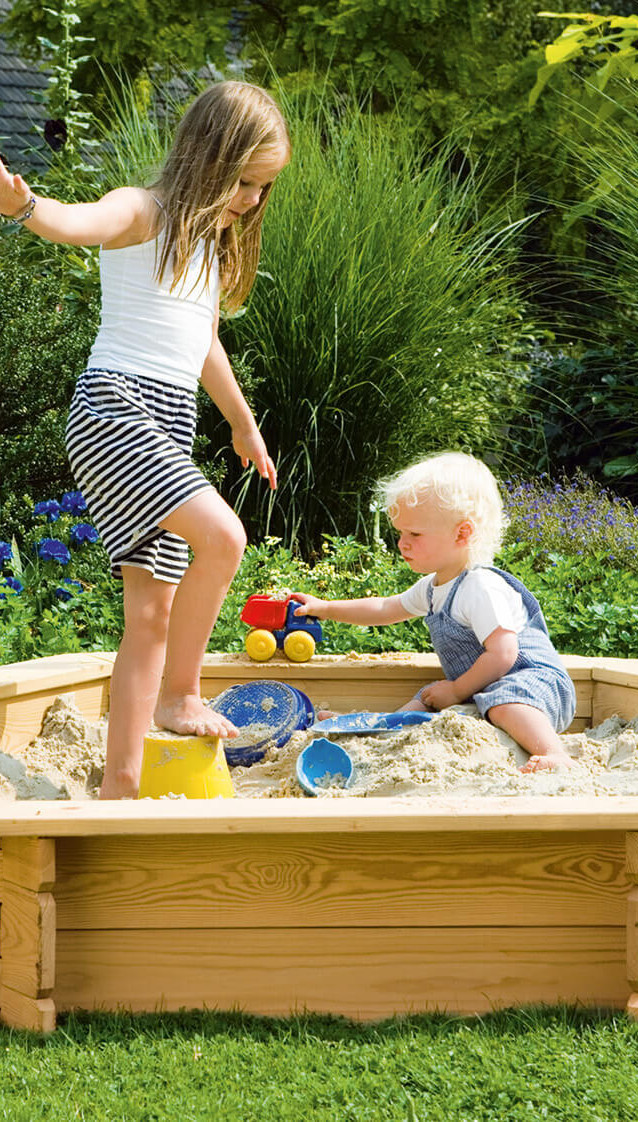 Kinder spielen in einem Sandkasten auf einer Wiese im Garten