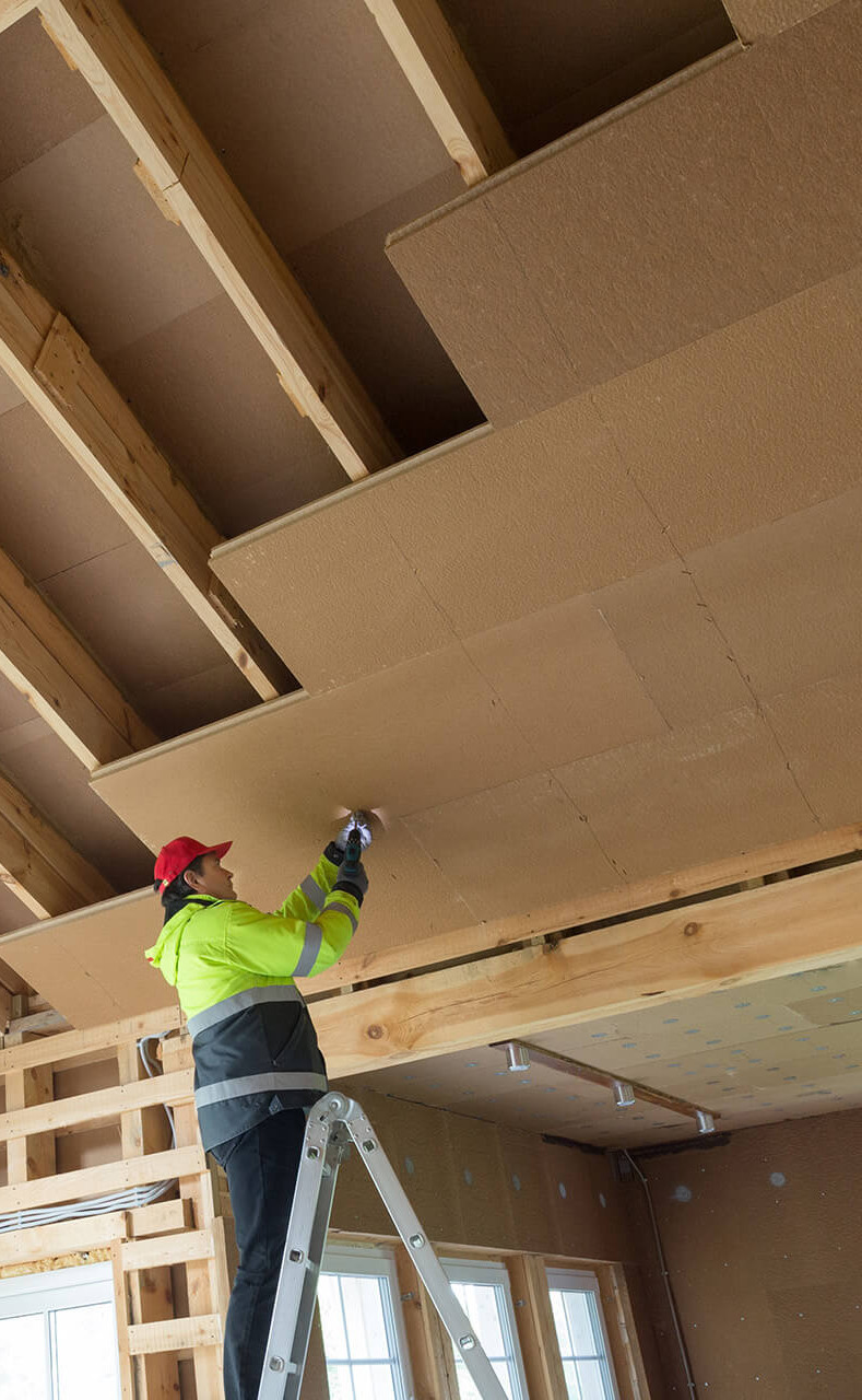 Handwerker montiert Faserdämmplatten am Dach eines Hauses