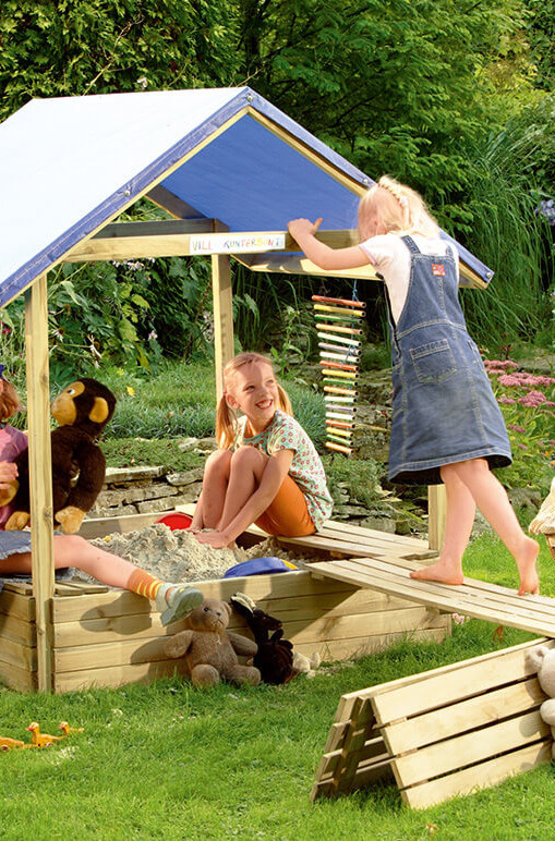 Kinder spielen in einem überdachten Sandkasten in einem Garten